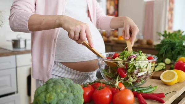 Terhes nő keveri a friss zöld salátát a konyhában. Közelkép. — Stock Fotó