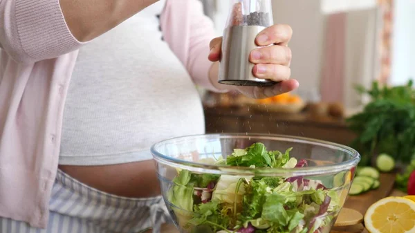 Těhotná žena solení salát na kuchyni. Closeup. — Stock fotografie