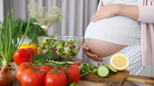 Těhotná žena připravuje zdravé jídlo na kuchyni. Detailní záběr na břicho. — Stock fotografie