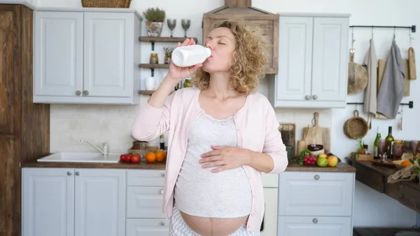 Gravid ung kvinna dricker yoghurt i köket. — Stockfoto