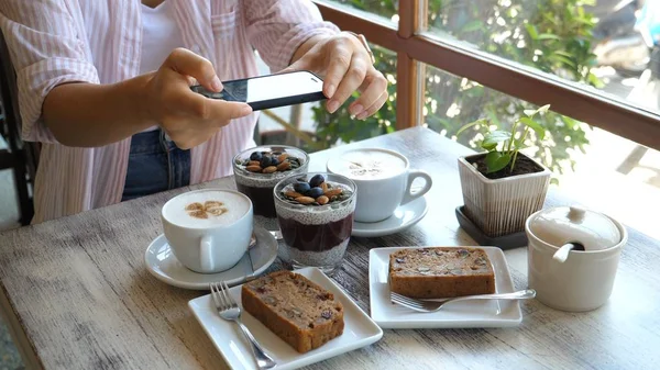Trendy meisje nemen van foto van veganistisch ontbijt met Chia, Bananenbrood en koffie met behulp van telefoon — Stockfoto