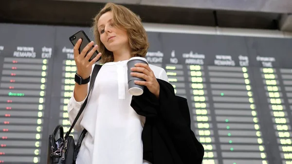 Молода ділова жінка використовує смартфон під час відправлення показу в аеропорту — стокове фото