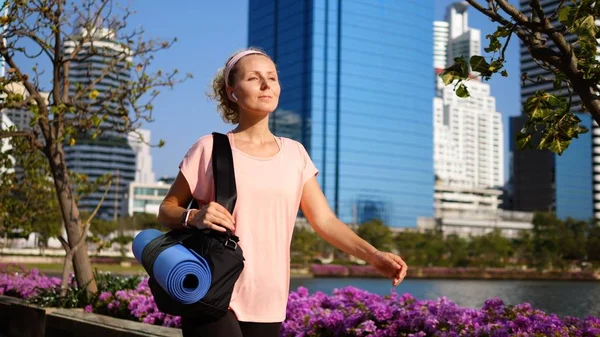 Mujer Fitness Caminando En El Parque De La Ciudad Con Estera De Yoga Usando Auriculares Inalámbricos —  Fotos de Stock