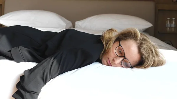 Уставшая деловая женщина, лежащая на кровати в номере отеля — стоковое фото
