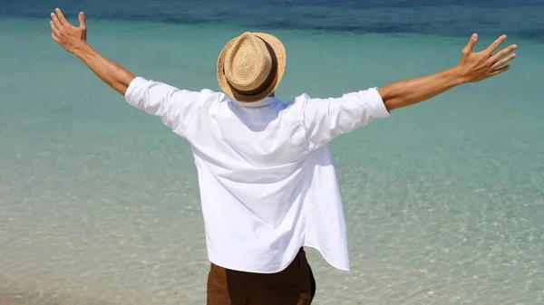 Erfolgreicher Mann hebt die Arme am Strand mit Blick auf das türkisfarbene Meer — Stockfoto