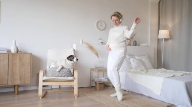 Kulaklıkla müzik dinleyen ve yatak odasında dans eden mutlu hamile kadın.