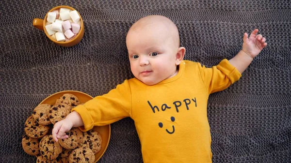 Funny Baby Boy acostado en punto a cuadros con galletas y chocolate caliente . —  Fotos de Stock