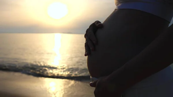 Silhouette di una donna incinta al tramonto in riva al mare . — Foto Stock