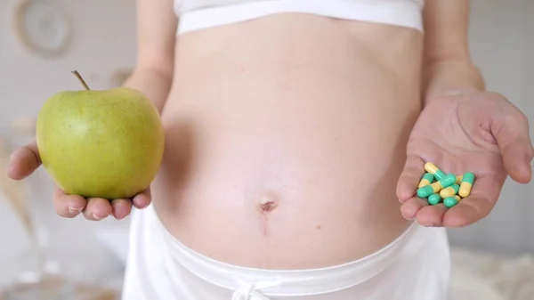 准妈妈拿着补药和青苹果。 Closeup Pregnant Belly 。 选择药丸或水果. — 图库照片