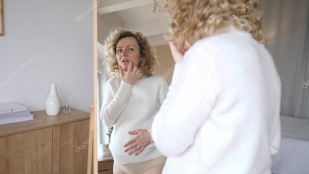 Disappointed And Upset Pregnant Woman Looking In Mirror At Her Problem Skin.