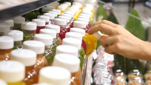 Женская рука выбирает свежий выжатый сок в пластиковой бутылке в супермаркете. Крупный план . — стоковое видео