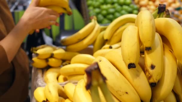 Kvinnlig kund väljer färsk frukt i en stormarknad. Närbild. Kvinnan väljer bananer. — Stockvideo