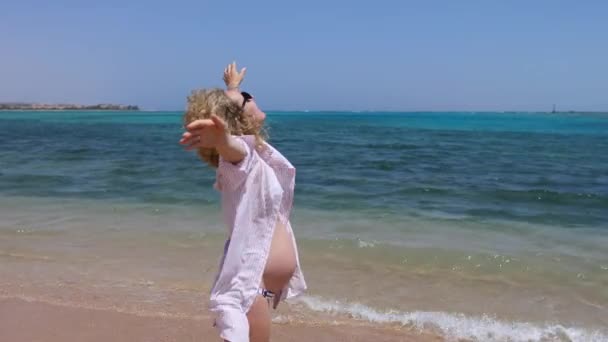 Ευτυχισμένη έγκυος γυναίκα με ανοιχτές αγκάλες στην παραλία δίπλα στη θάλασσα για διακοπές. — Αρχείο Βίντεο