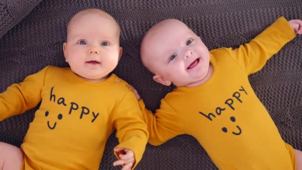 Twin Babies Wearing Happy Ochre T-Shirts And Lying On Knitted Blanket. Top View.