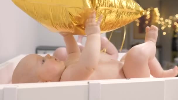 Bambino che gioca con il pallone d'oro. Bambini gemelli sdraiati sul fasciatoio senza pannolini . — Video Stock