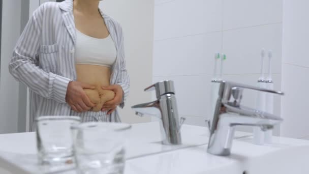 Frau mit Wochenbett-Bauch blickt im Badezimmer in den Spiegel. — Stockvideo