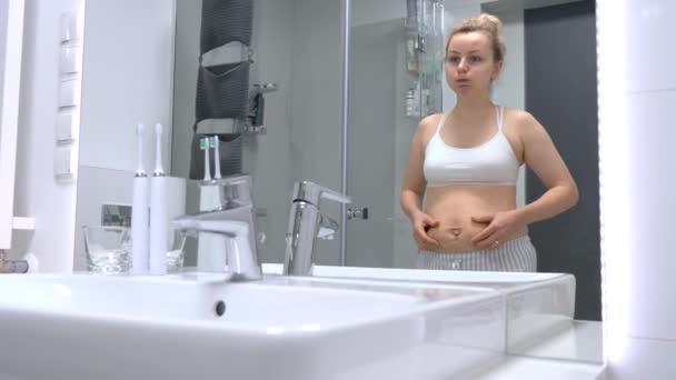 Mujer molesta mirando el espejo en su barriga posparto después del embarazo . — Vídeos de Stock