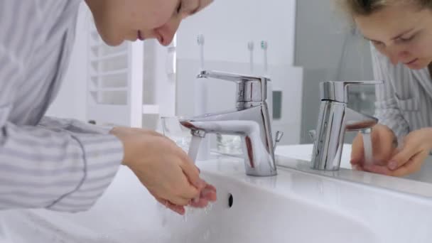 Jeune femme se laver le visage avec de l'eau debout dans la salle de bain . — Video