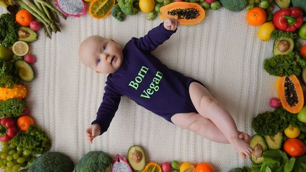 Bebé vegano acostado con verduras y frutas frescas crudas . — Foto de Stock