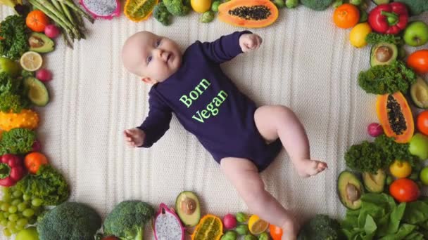 Bebé vegano acostado con verduras y frutas frescas crudas . — Vídeos de Stock