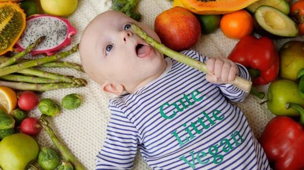 Lindo bebé vegano comiendo verduras frescas ecológicas de espárragos . — Foto de Stock