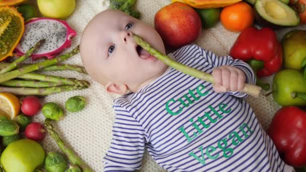 Lindo bebé vegano comiendo verduras frescas ecológicas de espárragos . — Vídeo de stock
