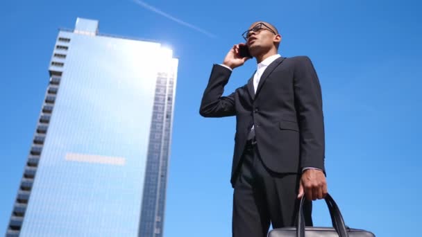 Hombre de negocios guapo con traje y anteojos hablando por teléfono cerca del edificio de oficinas . — Vídeos de Stock