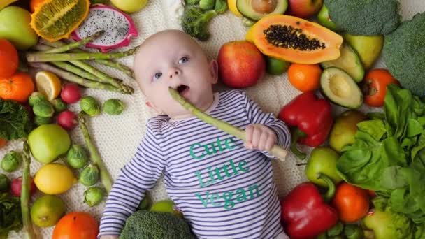 Meyve ve sebzelerin içinde yatan kuşkonmaz deneyen bebek. Sağlıklı Vegan Yaşam Tarzı. — Stok video