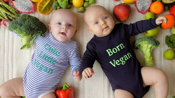 Bebé gemelos nacido vegano acostado en verduras frescas y frutas . — Foto de Stock