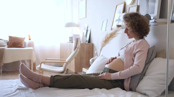 Концепция беременности. Беременная женщина сидит на кровати дома в спальне . — стоковое фото