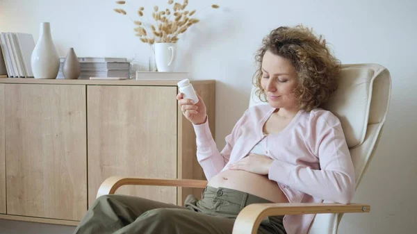 Mulher grávida segurando garrafa com medicina descansando em casa — Fotografia de Stock