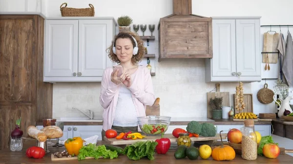 Zwangere vrouw koken gezond voedsel in de keuken en met behulp van Smartphone. — Stockfoto