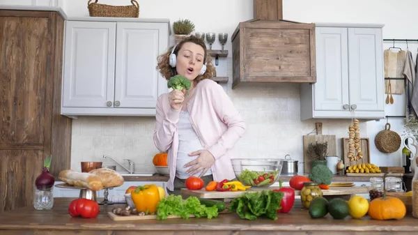 Happy Pregnancy. Pregnant Woman Singing In Broccoli And Dancing On Kitchen.