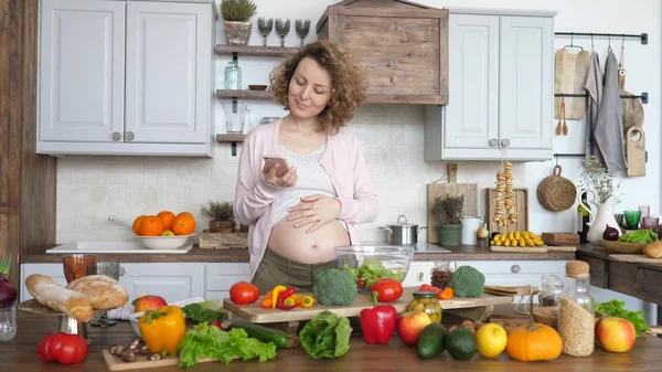 Молодая беременная женщина ищет рецепт на смартфоне и делает салат на кухне . — стоковое фото