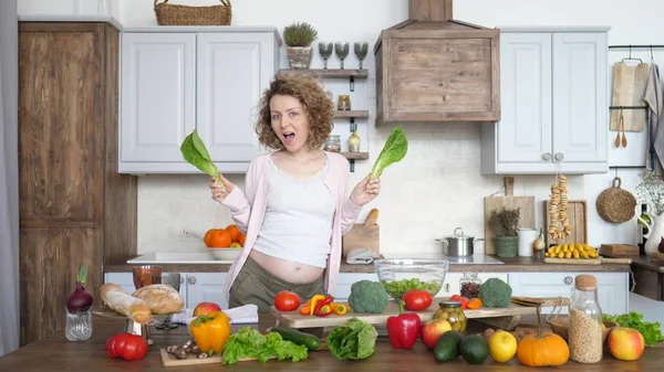 Счастливая беременность женщины, танцующей с зеленым салатом на кухне — стоковое фото