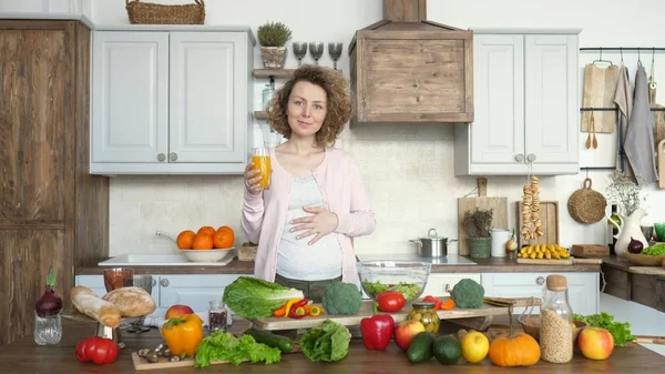 Ung gravid kvinna med glas apelsinjuice i köket — Stockfoto