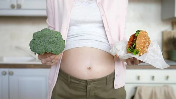 Hamilelik sırasında sağlıklı diyet. Hamile Kadın Burger ve Brokoli Tutuyor. — Stok fotoğraf