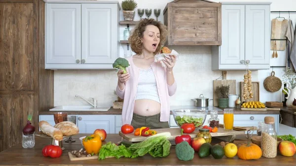 Skräp mat vs hälsosam mat. Gravid kvinna som håller Burger och Broccoli. — Stockfoto