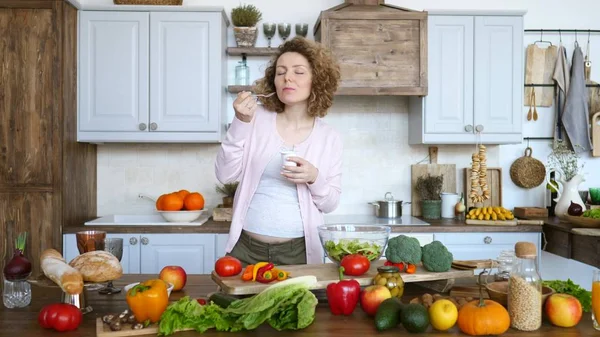 Zwangere vrouw die yoghurt eet in de keuken. Gezond voedselconcept. — Stockfoto