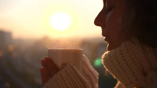 Žena drží horký šálek čaje nebo kávy venku při západu slunce. Útulná zimní koncepce. — Stock fotografie