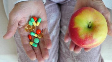 Closeup Of Elderly Female Hands Holding Apple And Pills.