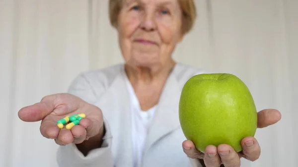 Eine ältere Frau hält Apfel und Pillen in den Händen. Nahaufnahme. — Stockfoto