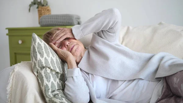 Öreg nő szenved fejfájás feküdt a kanapén — Stock Fotó