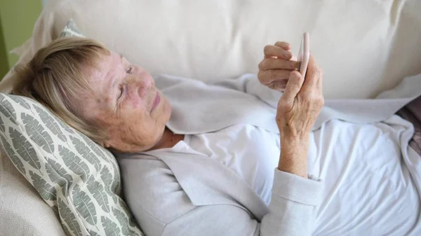 Großmutter entspannt auf Sofa mit Smartphone — Stockfoto