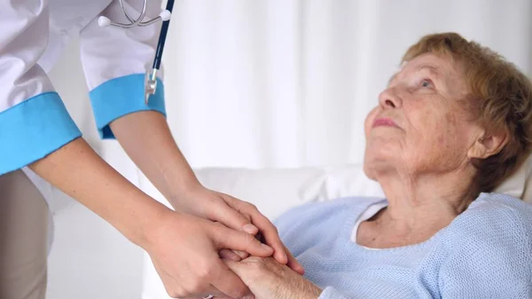 Doktor megnyugtatja az idősebb pácienseket, hogy fogják egymás kezét. Idősek egészségügyi ellátása. — Stock Fotó