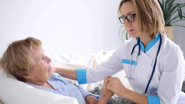 Ung doktor lugnar sin kvinnliga äldre patient hemma — Stockfoto