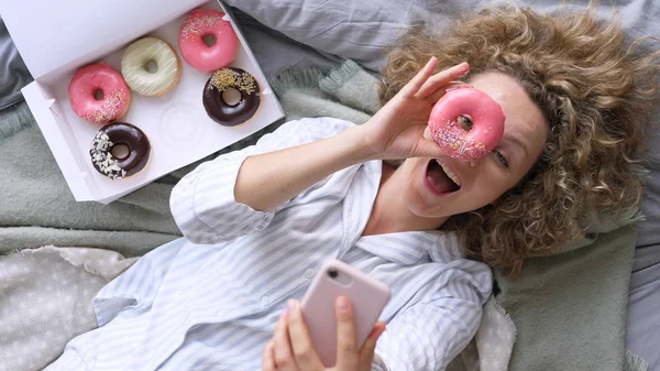 Joven mujer tomando selfie en cama con donuts — Foto de Stock