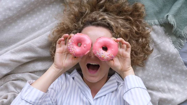 Joven mujer feliz con los ojos de rosquilla acostado en la cama — Foto de Stock