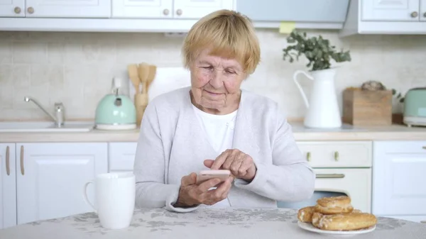 Портрет счастливой пожилой женщины с помощью смартфона на домашней кухне . — стоковое фото