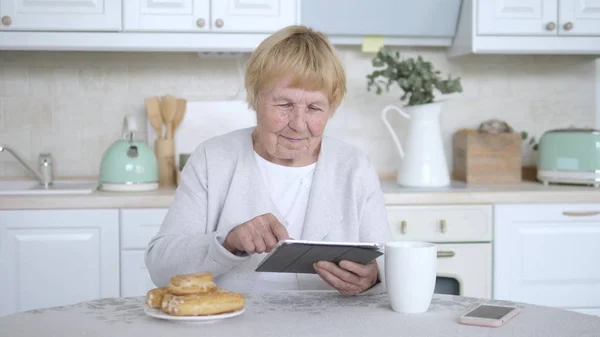 Bestemor som bruker nettbrett på kjøkkenet . – stockfoto